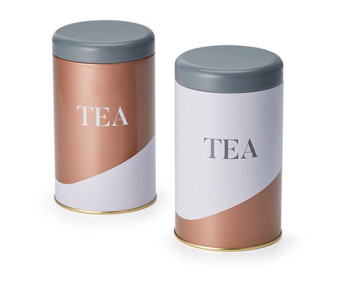 To stilfulde tedåser i hvid, bronze og grå med ordet Tea på